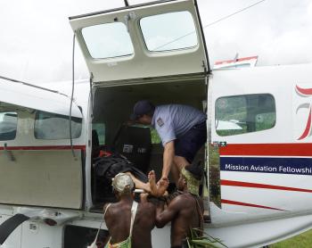 MAF Pilot Tim Neufeld loading a medevac patient onto an airplane with help from villagers.