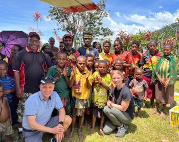 Stephanie Hald and David Berscheminski sits with a group of locals from Megau under the wing of the MAF aircraft