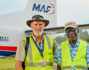 Two men stand in front of a plane