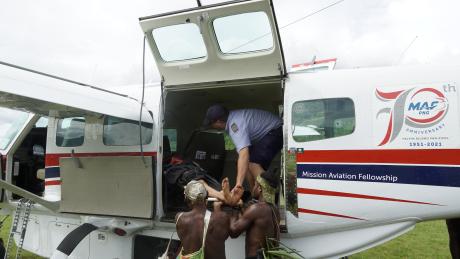 MAF Pilot Tim Neufeld loading a medevac patient onto an airplane with help from villagers.