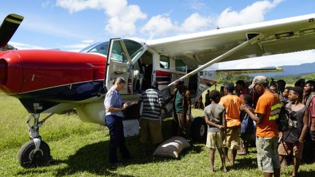 MAF Pilot Glenys Watson looking at flight paperwork as her plane gets loaded by locals.