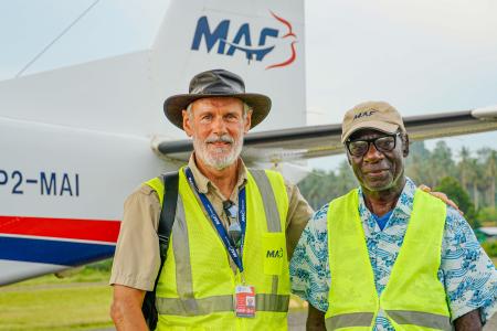 Two men stand in front of a plane