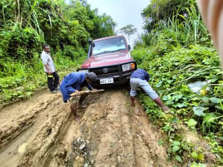 car bogged in the muddy road and people trying to get it out