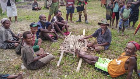 Dimanbil people sit around a stretcher they have made to move dirt from the runway excavation. 