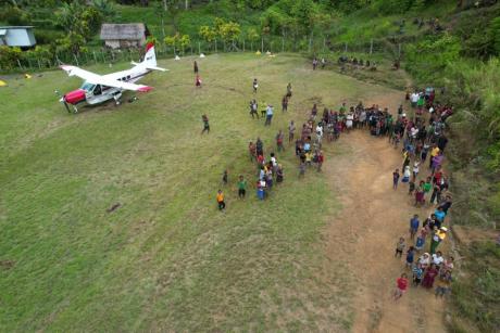An MAF plane on a remote airstrip with crowd of village people 