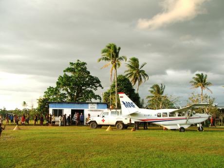 A plane on a grass airstrip with ambulance and local people watching