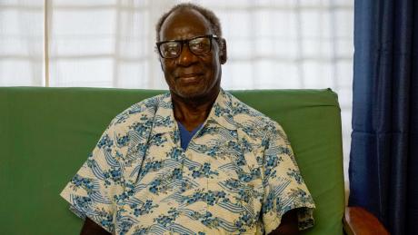 a man with glasses sits on a couch smiling